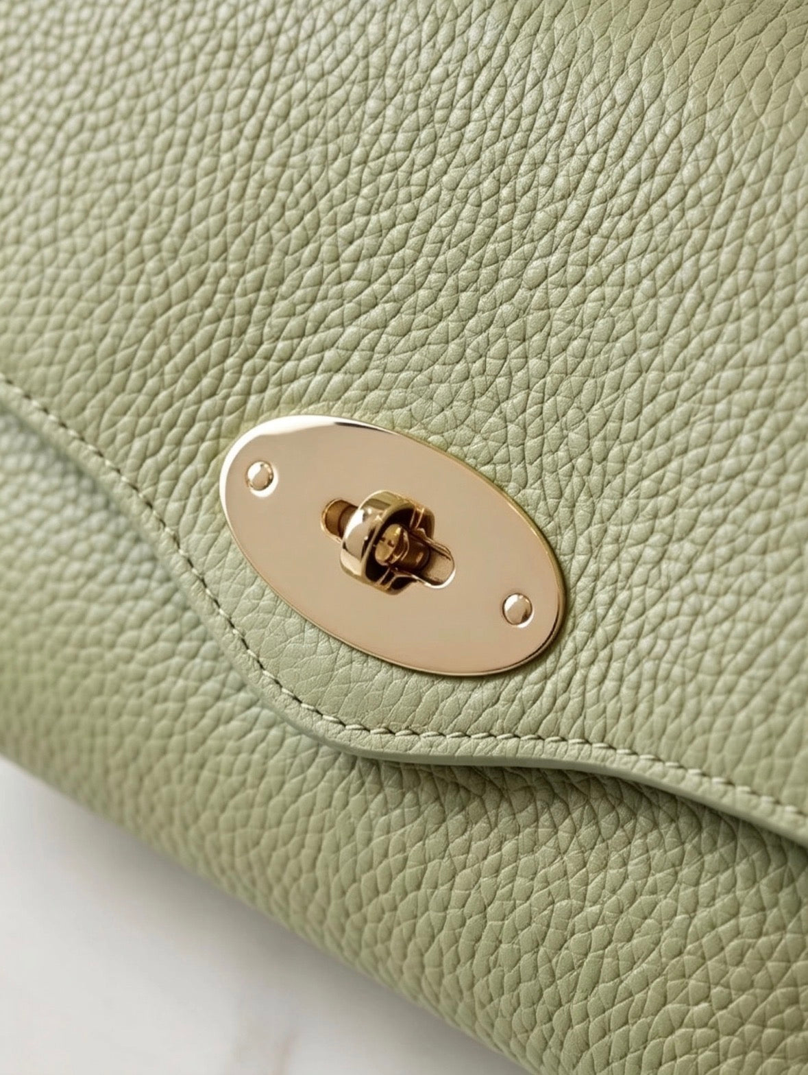 Close-up of gold oval turn-lock clasp on Italian handmade genuine leather mini top handle crossbody bag in sage olive