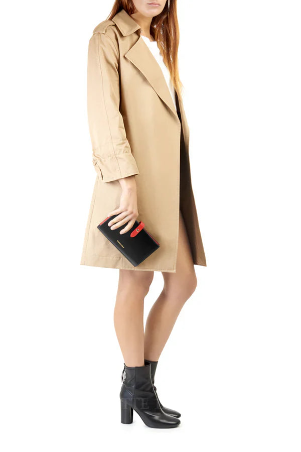 Model image: Woman in camel trench coat holding an Italian genuine leather continental wallet in black with red tab closure | MERLEORA